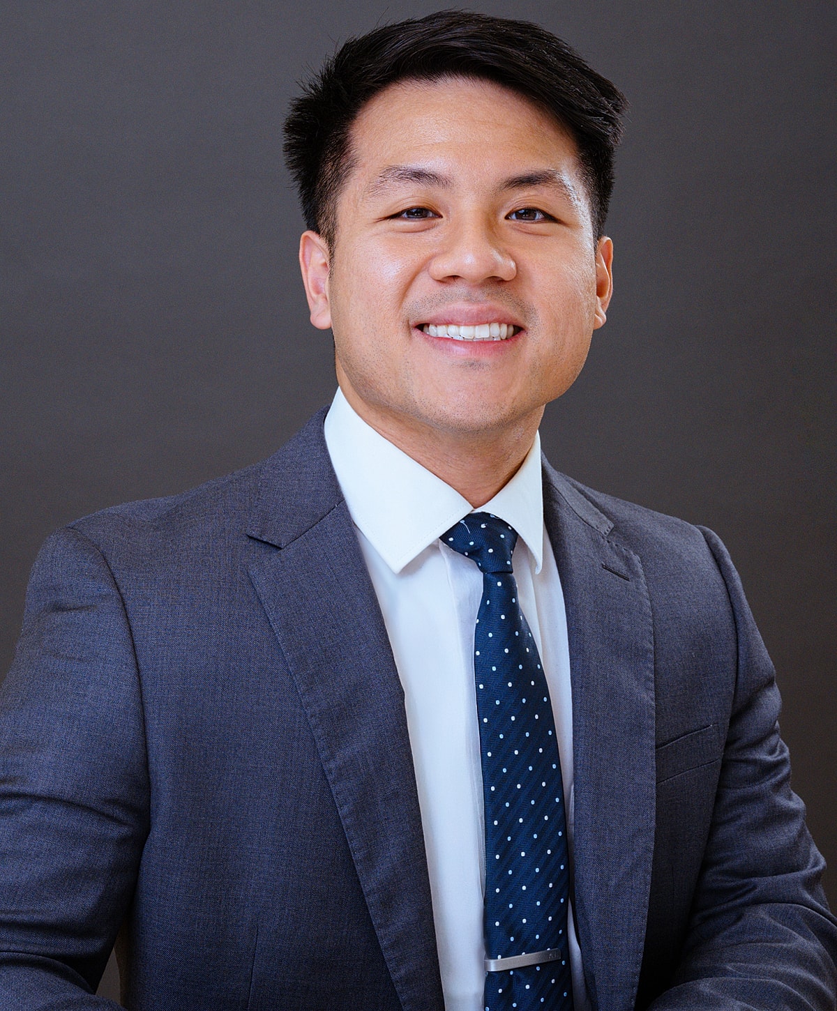 Smiling man in a suit against a dark background.